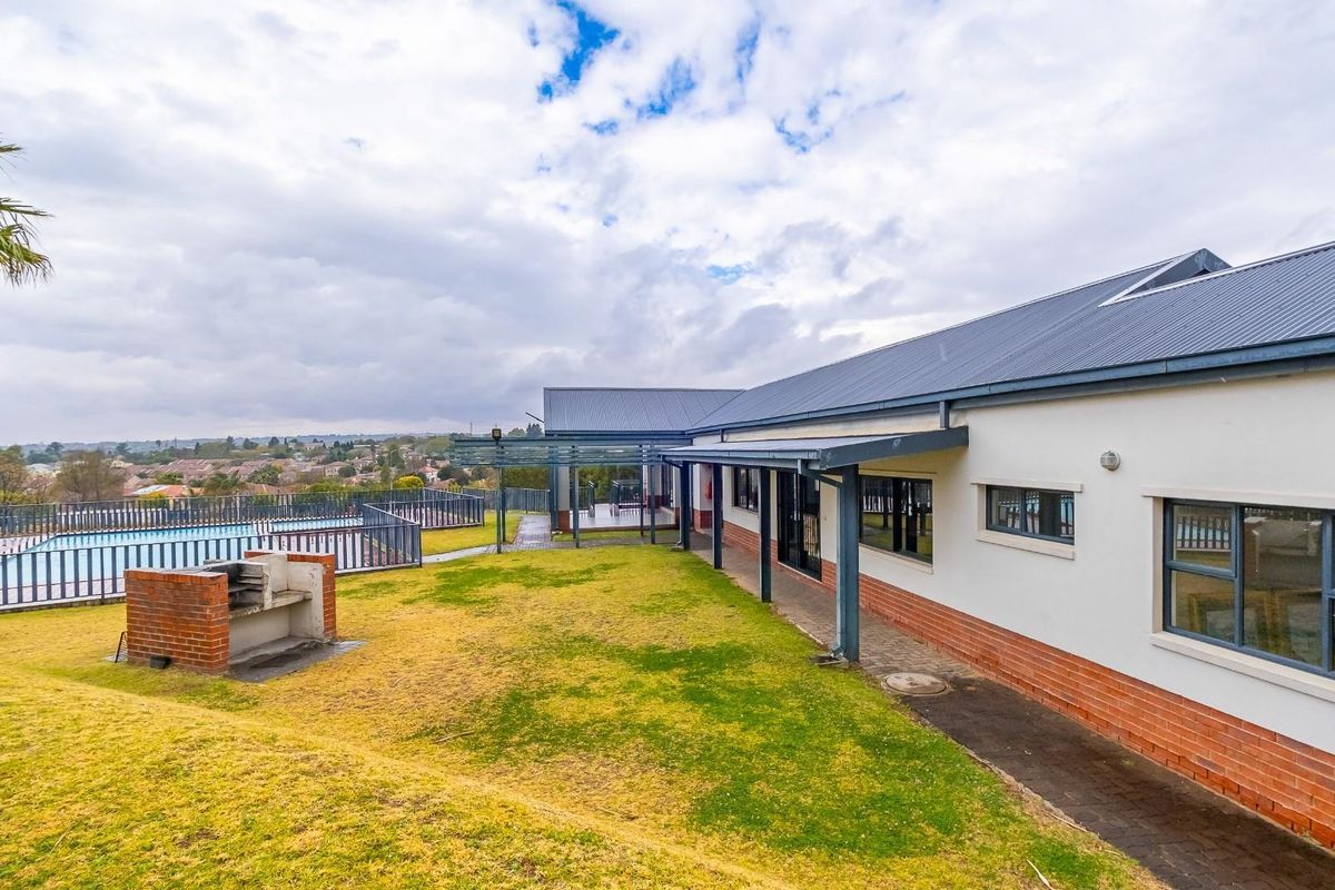 Rear exterior view featuring a swimming pool, a brick built-in braai, a covered patio area, and a well-maintained lawn with surrounding fencing.