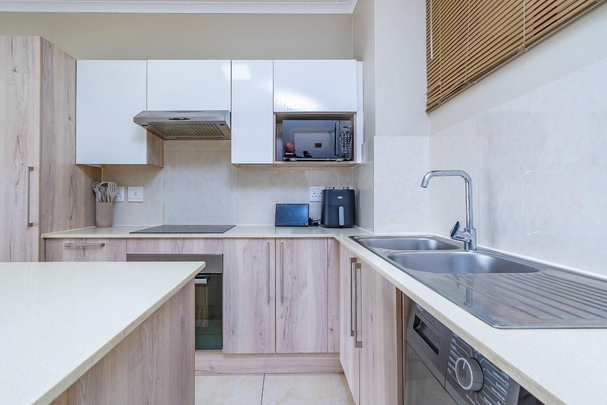 Modern kitchen featuring light wood-tone cabinetry, white upper cabinets, integrated appliances, and a functional double sink with a tiled backsplash.