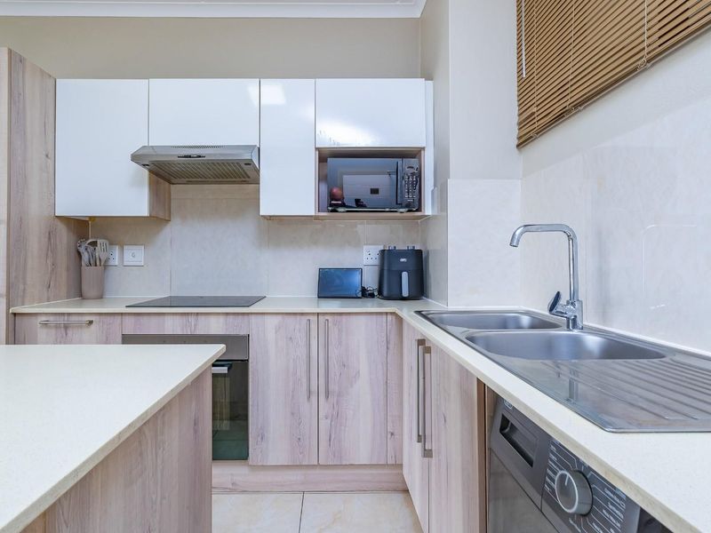Modern kitchen featuring light wood-tone cabinetry, white upper cabinets, integrated appliances, and a functional double sink with a tiled backsplash.