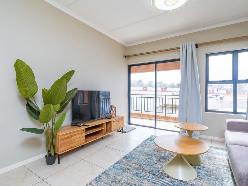 A bright living room featuring tiled flooring and a sliding glass door that opens onto a balcony, providing natural light and outdoor access.