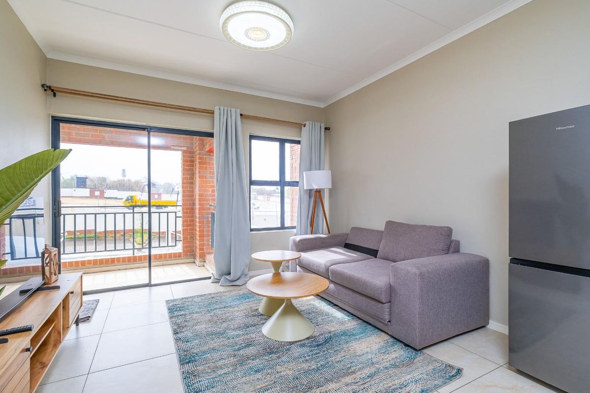 A bright living room featuring tiled flooring, a ceiling light fixture, and a sliding glass door providing access to an outdoor balcony area.