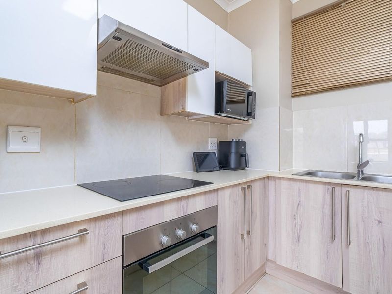 Modern kitchen featuring light wood-grain cabinetry, stone countertops, built-in oven, electric hob, extractor fan, and a stainless steel sink with tiled splashback.