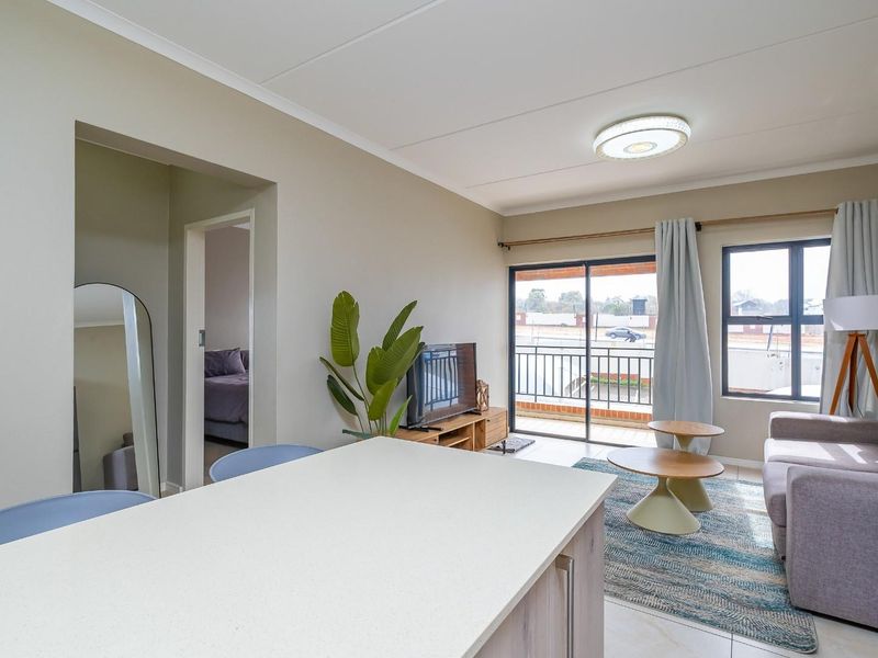 Bright open-plan living area featuring tiled flooring, a kitchen island, and a sliding glass door leading to a balcony.