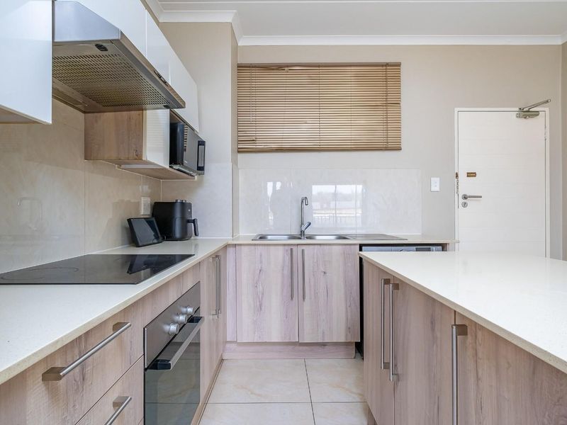 Modern kitchen featuring light wood-grain cabinetry, stone countertops, integrated electric hob, oven, extractor fan, and a functional double sink layout.