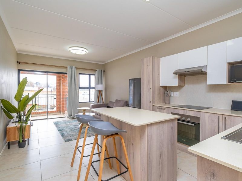Modern open-plan apartment featuring a well-equipped kitchen with built-in appliances, a central island, and seamless flow to a private balcony.