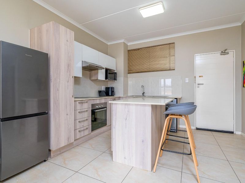 Modern kitchen featuring light wood-finish cabinetry, a central island, integrated appliances, and tiled flooring, offering a clean and functional cooking space.