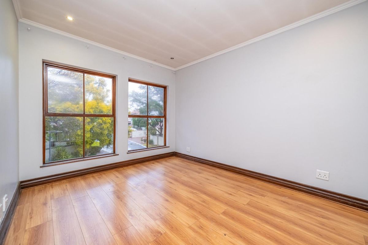 A bright, empty bedroom featuring laminate flooring, timber-framed windows, and neutral wall finishes, offering a clean canvas for personalization.