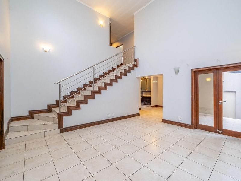 Spacious entrance hall featuring a staircase with a stainless steel balustrade, tiled flooring, and direct access to adjacent living areas.