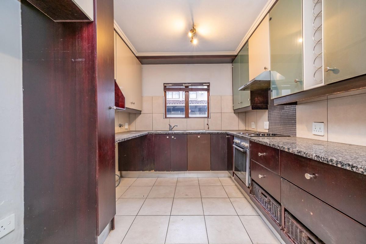 A functional kitchen featuring dark wood cabinetry, granite countertops, built-in oven and hob, and tiled flooring, offering a practical layout for culinary activities.