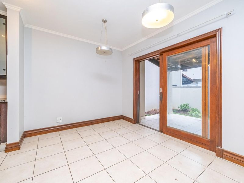 An empty dining area featuring tiled floors, pendant lighting, and a large timber-framed sliding door providing direct access to the patio.