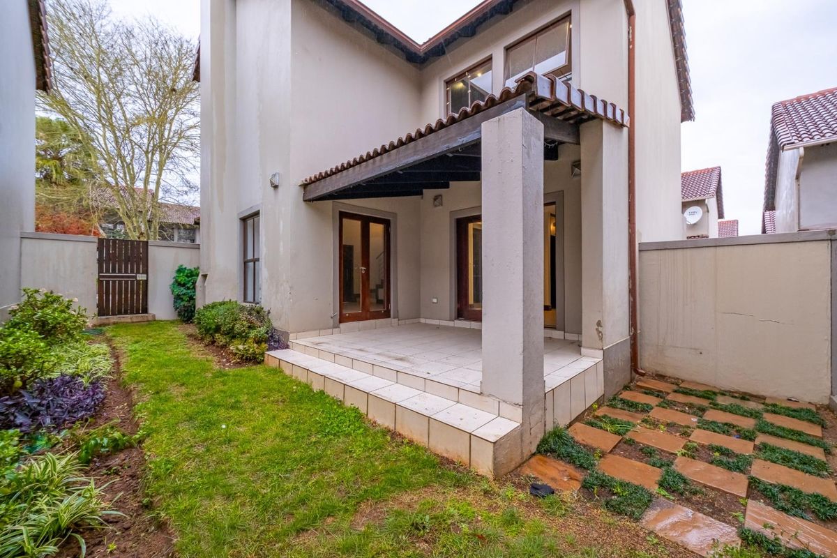 Rear view of the townhouse featuring a covered tiled patio, timber pergola, and a private garden area with boundary walls.