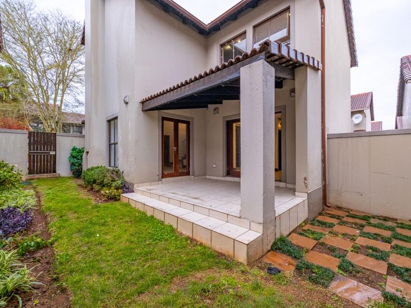 Rear view of the townhouse featuring a covered tiled patio, timber pergola, and a private garden area with boundary walls.
