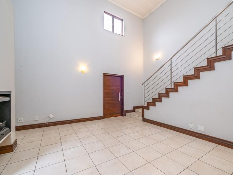 Spacious living area featuring high ceilings, a built-in fireplace, tiled flooring, and a staircase with a modern stainless steel balustrade.
