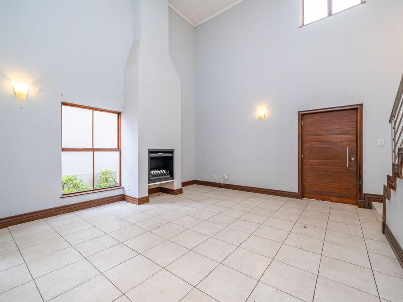 Spacious living area featuring high ceilings, tiled flooring, a built-in fireplace, and a wooden entrance door with an adjacent staircase.