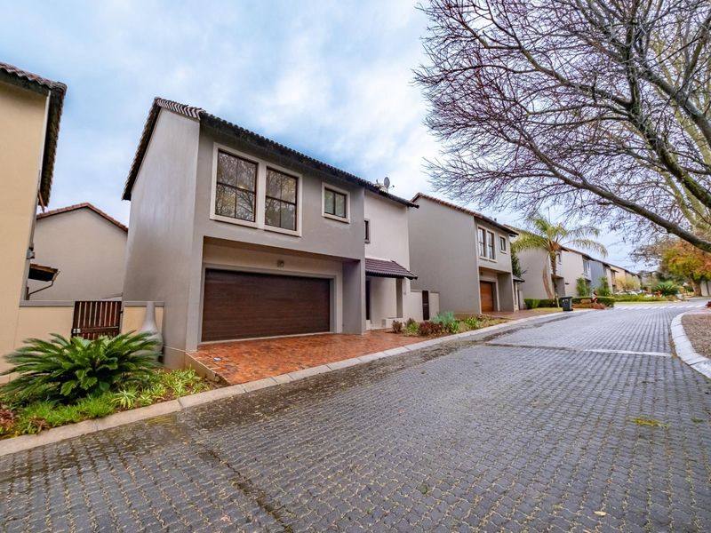 Front elevation of a modern townhouse featuring a double garage, paved driveway, and well-maintained exterior finishes within a residential complex.