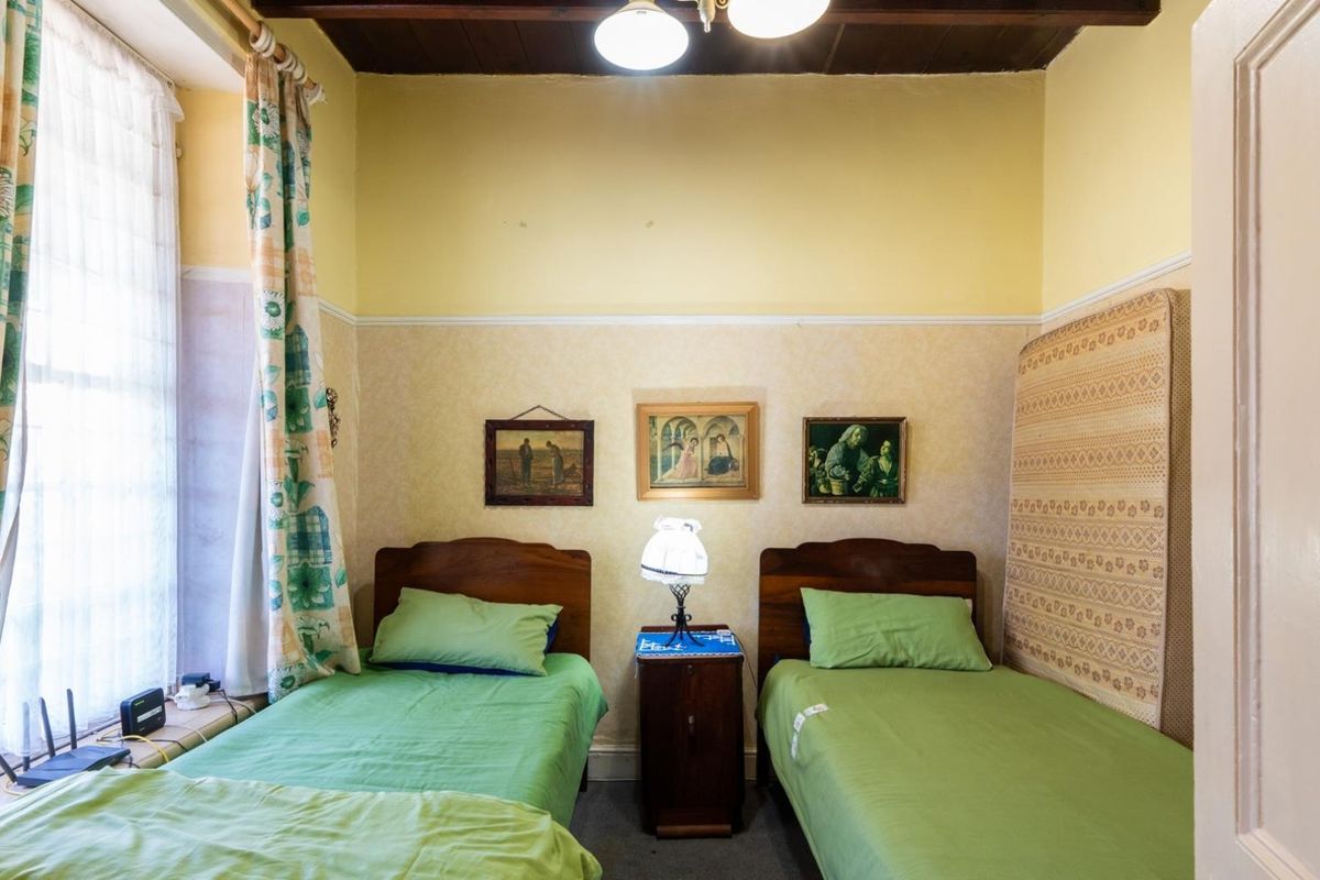 A bedroom featuring exposed timber ceiling beams and a large sash window, offering a dated aesthetic ready for modernization.