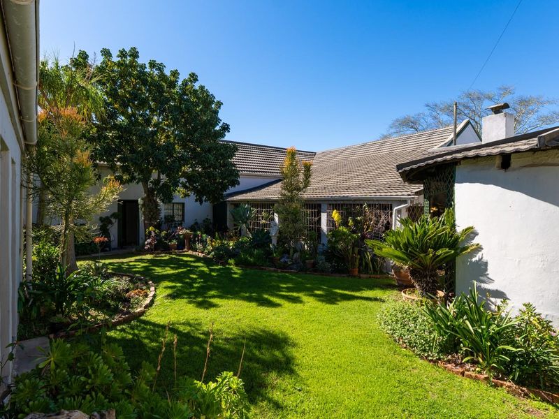 A well-maintained rear garden area featuring a lush lawn, established greenery, and a view of the property's rear facade with tiled roofing.