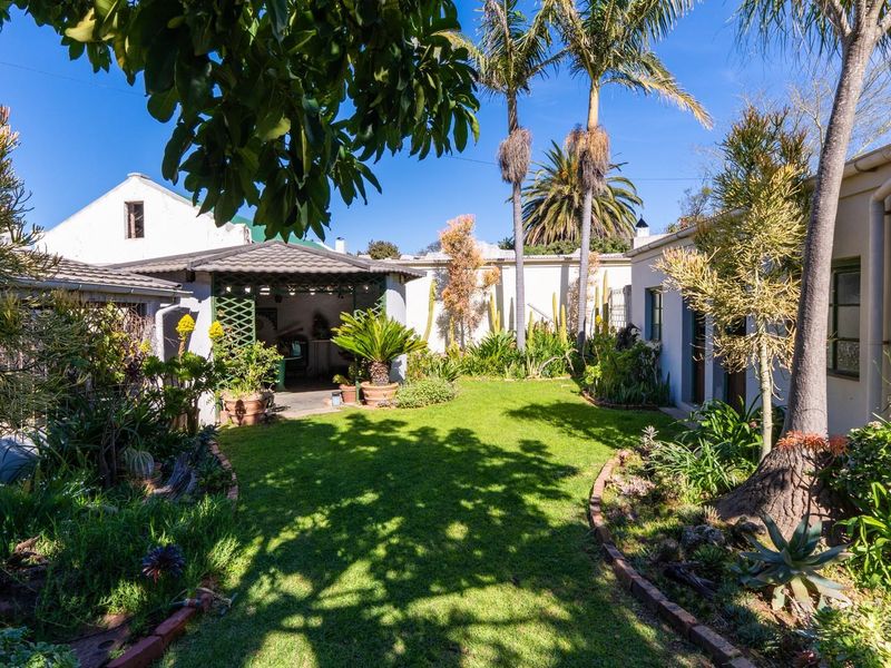 A well-maintained rear garden featuring a lush lawn, established landscaping, and a covered patio area perfect for outdoor relaxation.