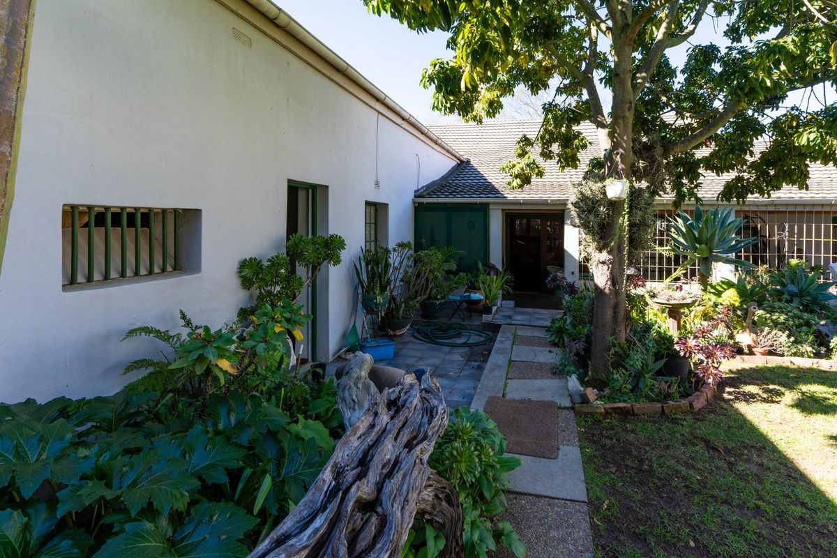 A rear garden view featuring a paved walkway leading to a covered patio area with established landscaping and mature trees.