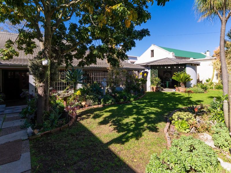 A well-maintained rear garden featuring a lush lawn, established trees, brick-edged garden beds, and a covered patio area attached to the main house.