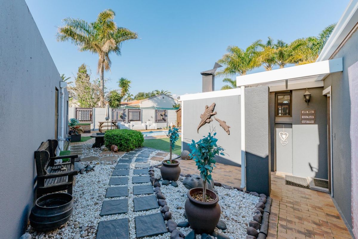 A well-maintained rear courtyard featuring a paved walkway, decorative landscaping, and a swimming pool area with an outdoor chimney.