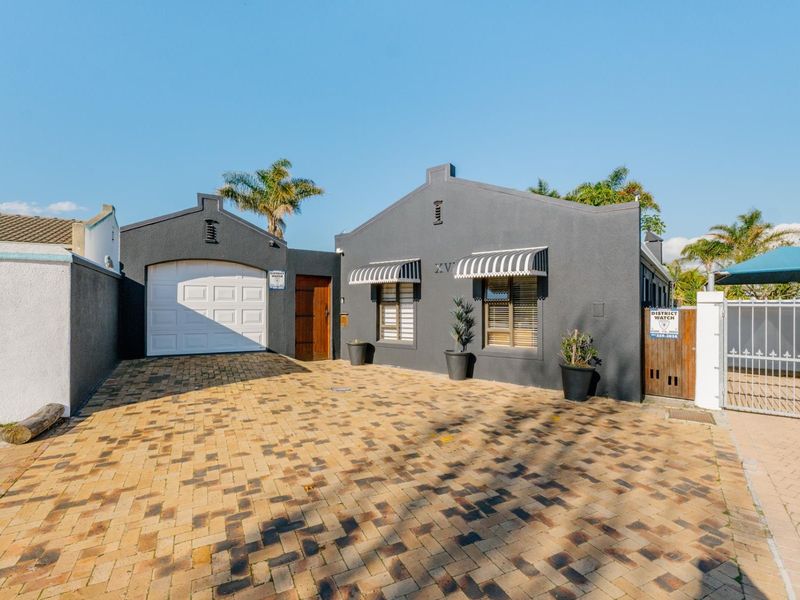 Front elevation of a modern house featuring a paved driveway, single garage, and secure gated entrance with striped window awnings.