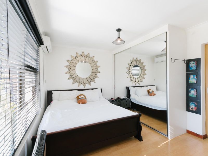 A well-maintained bedroom featuring laminate flooring, a large mirrored built-in wardrobe, split-system air conditioning, and venetian blinds.