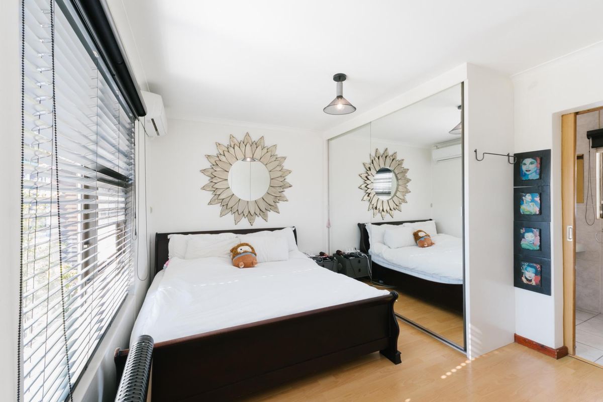 A well-maintained bedroom featuring laminate flooring, a large mirrored built-in wardrobe, split-system air conditioning, and venetian blinds.