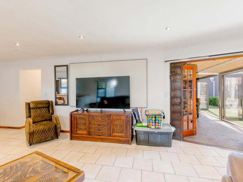 Spacious living room featuring tiled flooring, recessed downlights, and folding timber doors providing seamless access to the outdoor patio area.