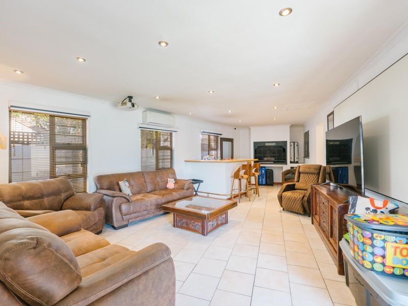 Spacious open-plan living area featuring tiled floors, recessed lighting, a built-in bar, and an indoor braai, ideal for entertaining.