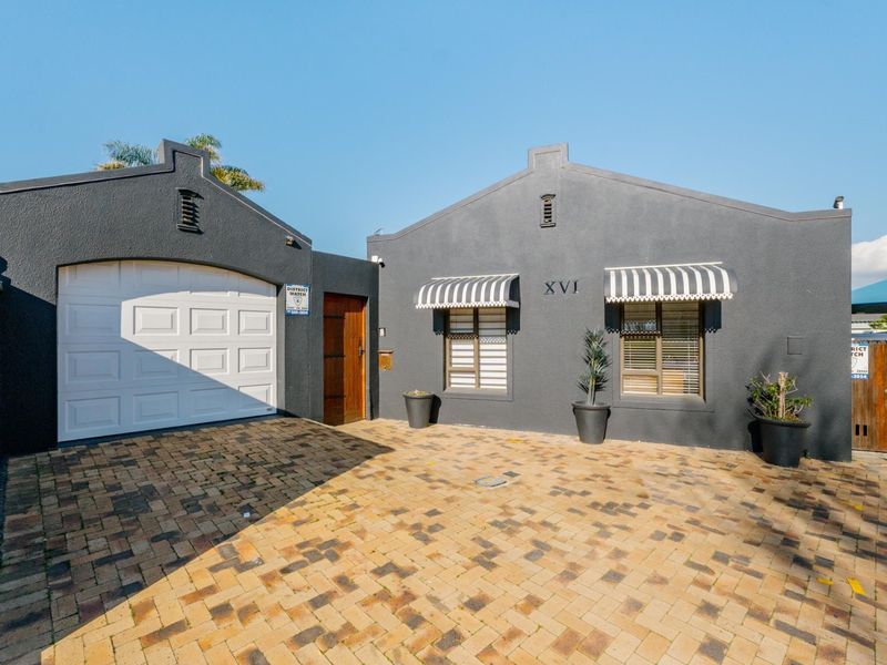 Front exterior view of the property featuring a paved driveway, single garage, and dark grey facade with striped window awnings.