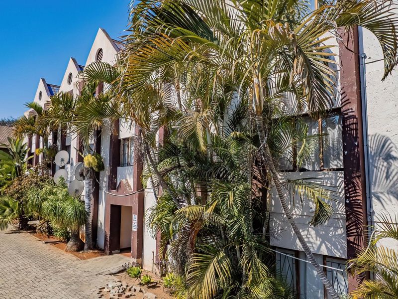 Exterior view of an apartment complex featuring a paved driveway, mature palm trees, and a multi-story facade with gabled architectural details.