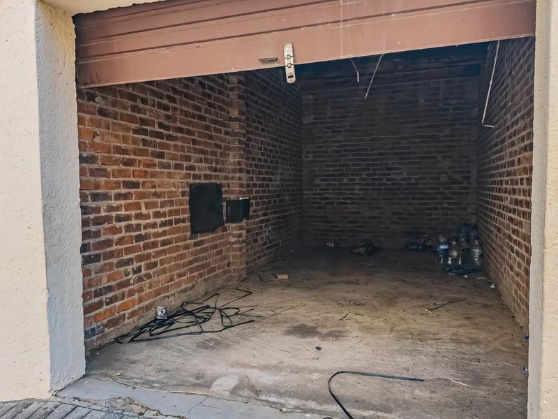 A vacant, single-car garage featuring exposed brick walls and a concrete floor, requiring maintenance and cleanup.