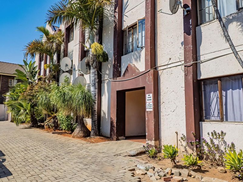 Exterior view of an apartment building facade featuring paved driveway access, security bars on windows, and multiple satellite dish installations.