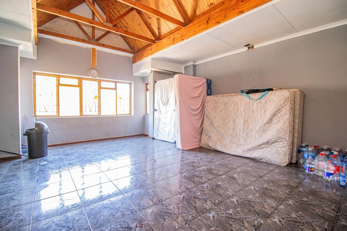 Spacious living area featuring exposed timber roof trusses, tiled flooring, and large windows, offering a blank canvas for renovation and interior design.