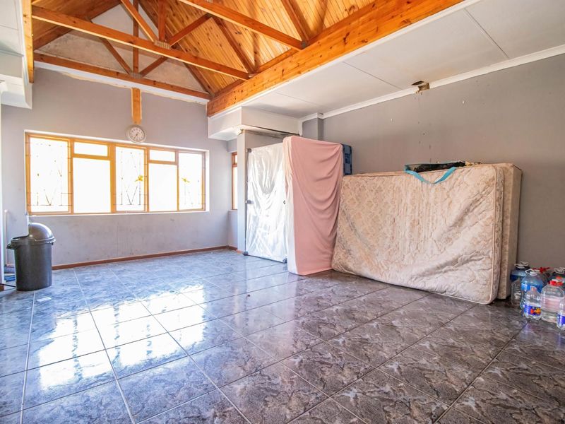 Spacious living area featuring exposed timber roof trusses, tiled flooring, and large windows, offering a blank canvas for renovation and interior design.