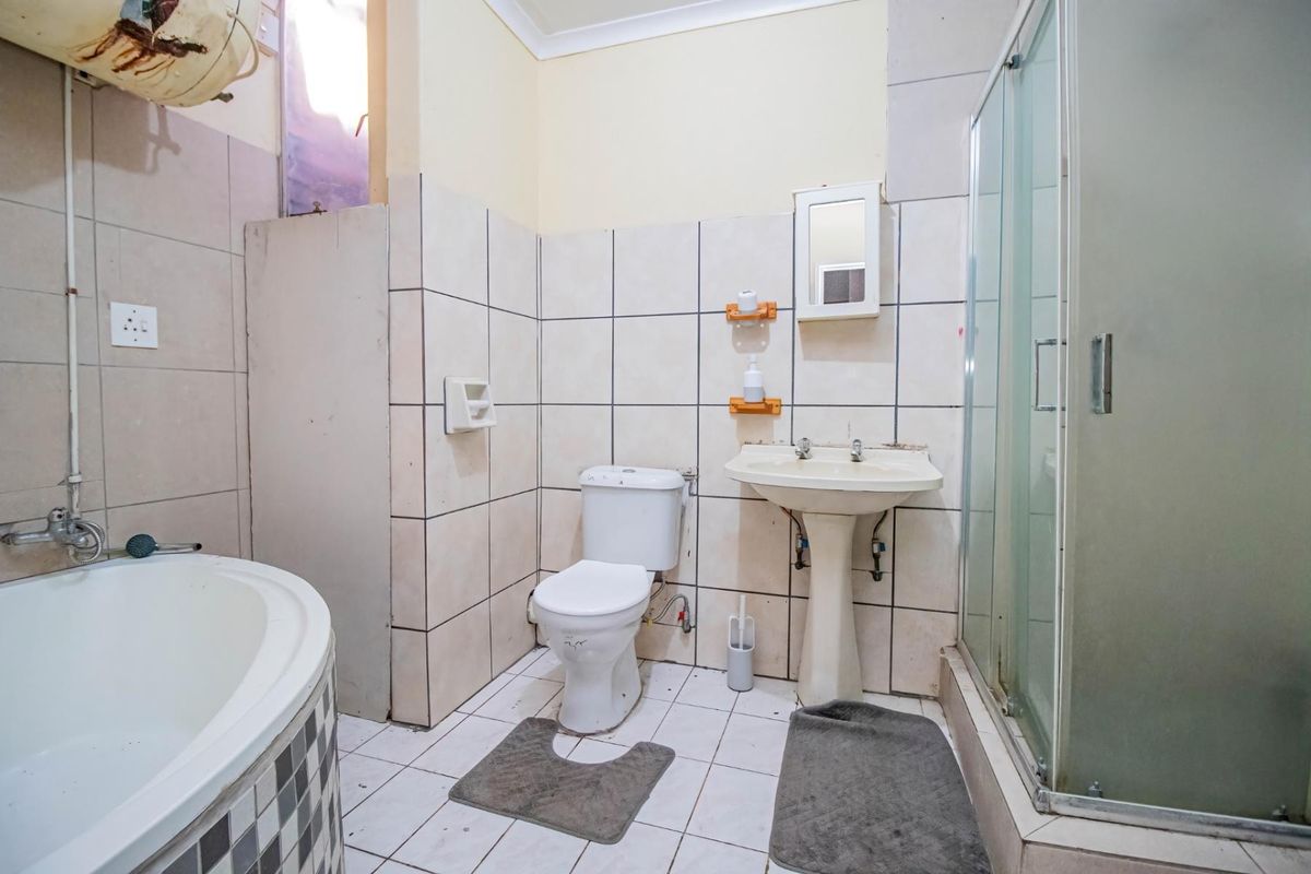 A dated bathroom featuring a corner bathtub, separate shower enclosure, pedestal basin, and toilet, requiring cosmetic updates and maintenance to improve its overall condition.