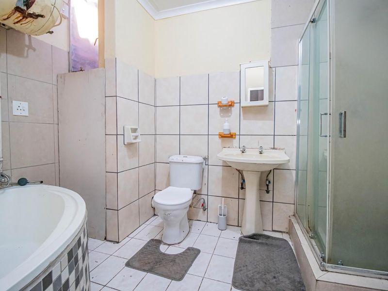 A dated bathroom featuring a corner bathtub, separate shower enclosure, pedestal basin, and toilet, requiring cosmetic updates and maintenance to improve its overall condition.