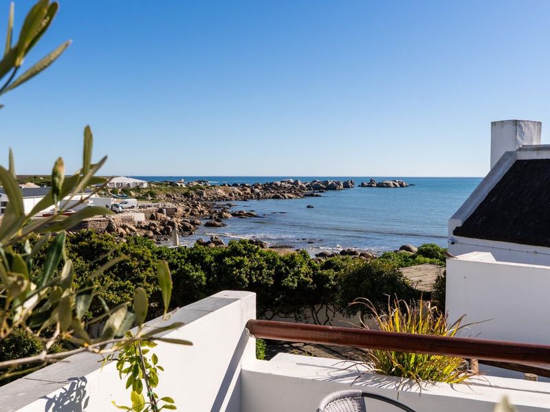 A scenic elevated view overlooking the rocky coastline and ocean, featuring a glimpse of a traditional thatched roof property.