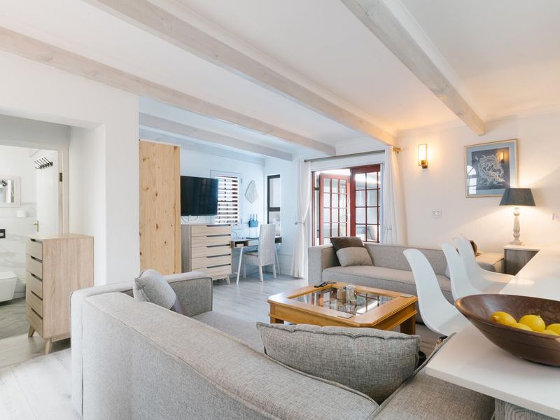 A bright open-plan living and kitchen area featuring exposed timber ceiling beams, neutral finishes, and direct access to an outdoor space through french doors.