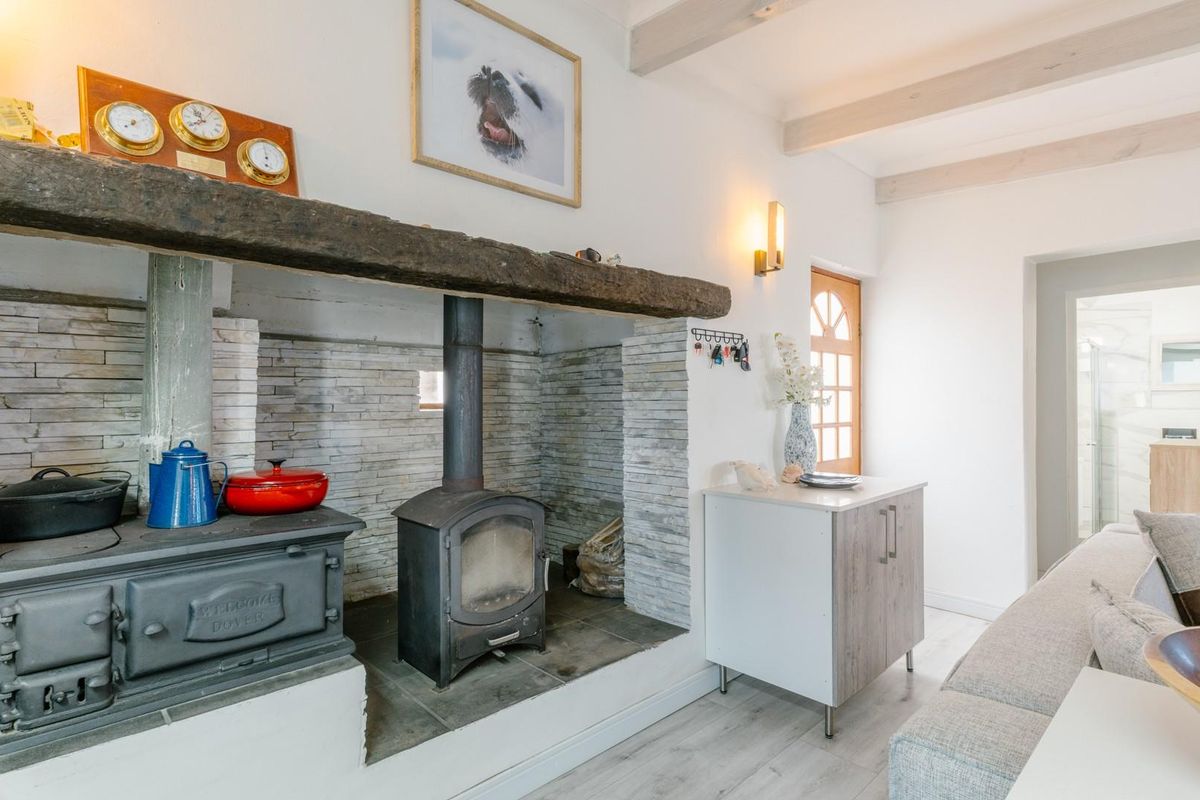 Cozy living area featuring a prominent stone fireplace with a wood-burning stove, timber mantelpiece, and exposed ceiling beams, creating a warm, rustic atmosphere.