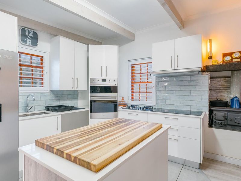 Modern kitchen featuring white cabinetry, subway tile backsplash, built-in appliances, a central island, and a rustic cast iron stove set into a stone hearth.