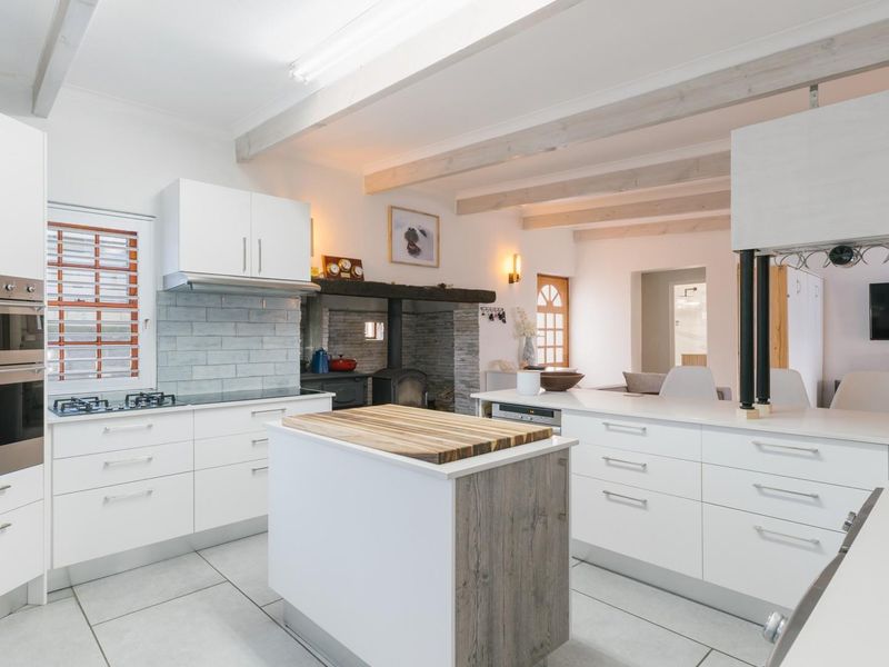 Modern kitchen featuring white cabinetry, a central island with wood-top, built-in appliances, subway tile backsplash, and exposed ceiling beams with an integrated fireplace.