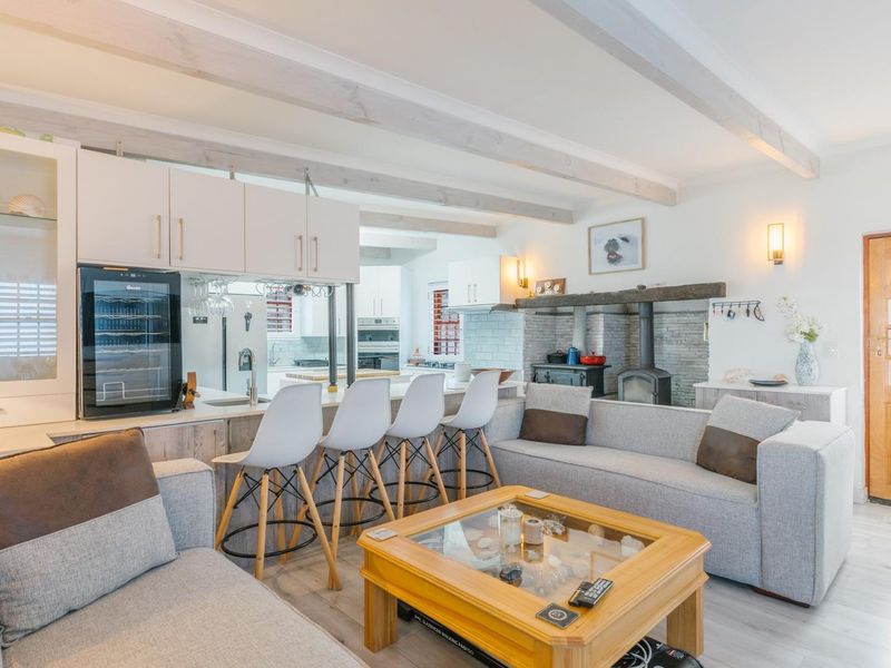 Spacious open-plan living area featuring exposed ceiling beams, a cozy wood-burning fireplace with stone surround, and a modern kitchen with integrated cabinetry.