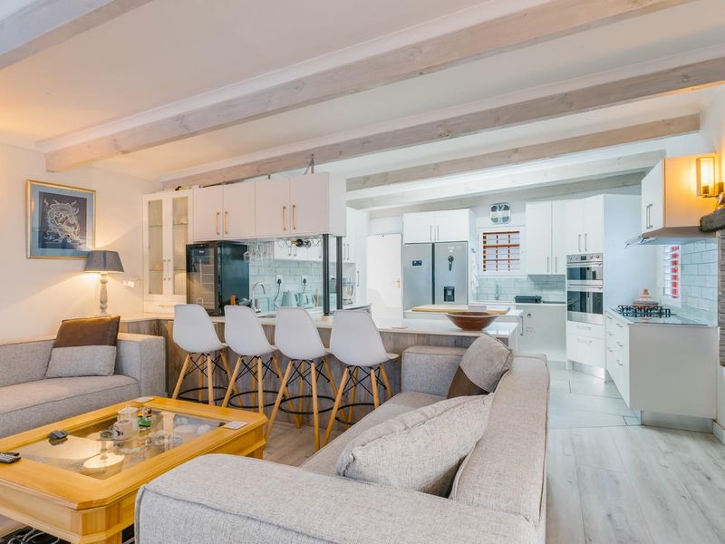 Spacious open-plan living area featuring exposed timber beams, a modern kitchen with a central island, and a cozy stone fireplace.
