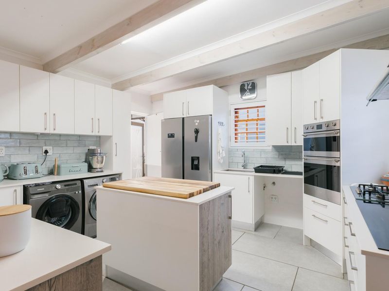 Modern kitchen featuring white cabinetry, a central island, double wall oven, gas cooktop, and stylish tiled backsplash with exposed ceiling beams.