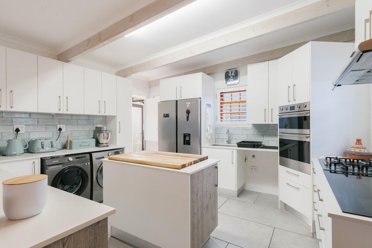 Modern kitchen featuring white cabinetry, a central island, double wall oven, gas cooktop, and stylish tiled backsplash with exposed ceiling beams.