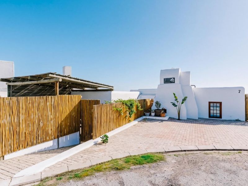 Front exterior view of the property featuring a paved driveway, bamboo privacy fencing, and a covered timber pergola entrance.