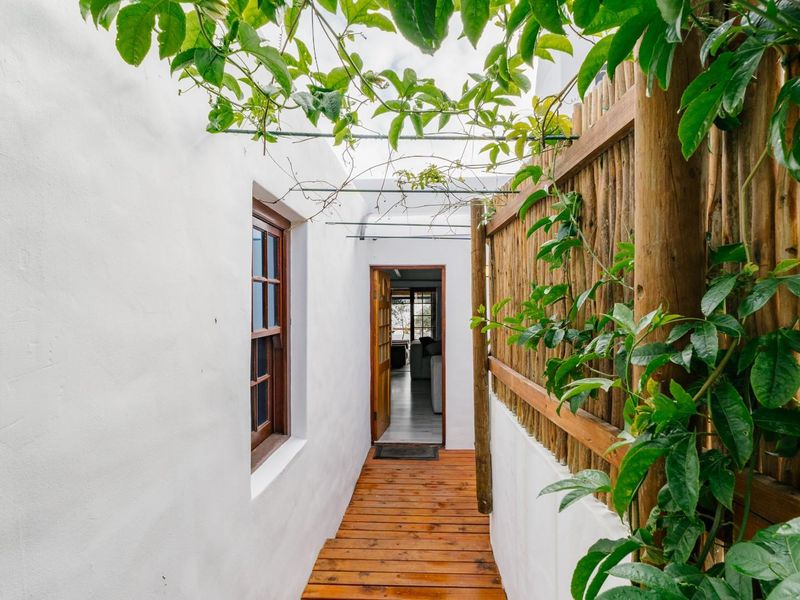 A narrow outdoor walkway featuring timber decking, a rustic wooden screen fence, and a pergola structure leading to the main entrance.