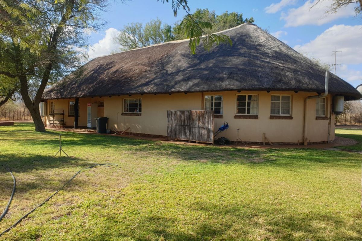 Rear view of a traditional farmhouse featuring a thatched roof, plastered exterior walls, and established garden surroundings.